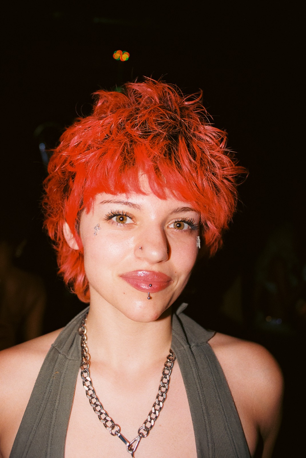 Close-up film portrait of a girl with a red pixie cut and chain necklace